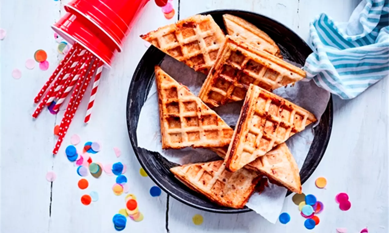 Golden triangular waffle slices with pizza-style toppings arranged on white parchment paper in a black plate on a wooden table