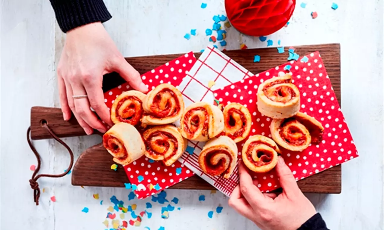 Golden pizza swirls with a flaky crust and spirals of red filling arranged on red polka-dot napkins on a wooden board